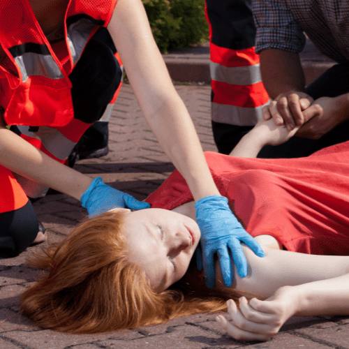 A woman wearing blue gloves provides first aid to a patient on the ground.
