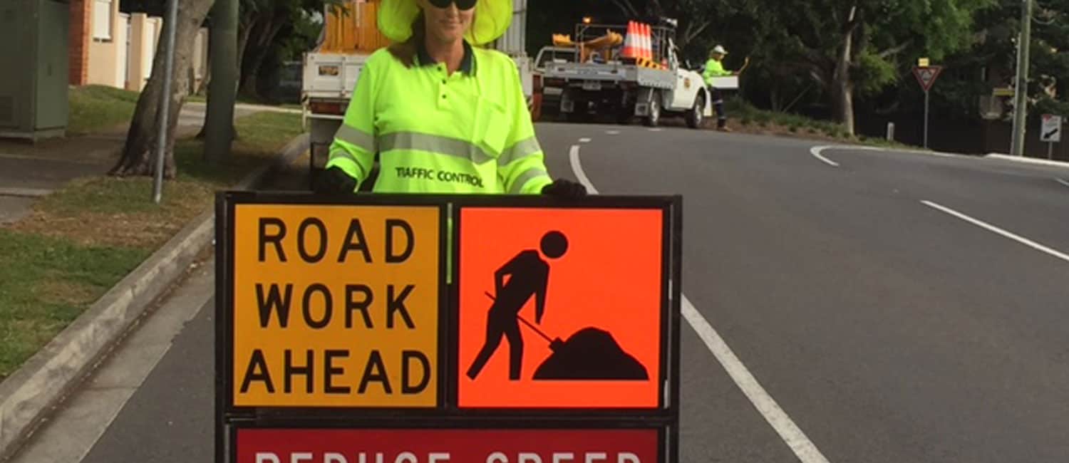 A road worker next to a road work ahead sign as part of Traffic Management Implementation.