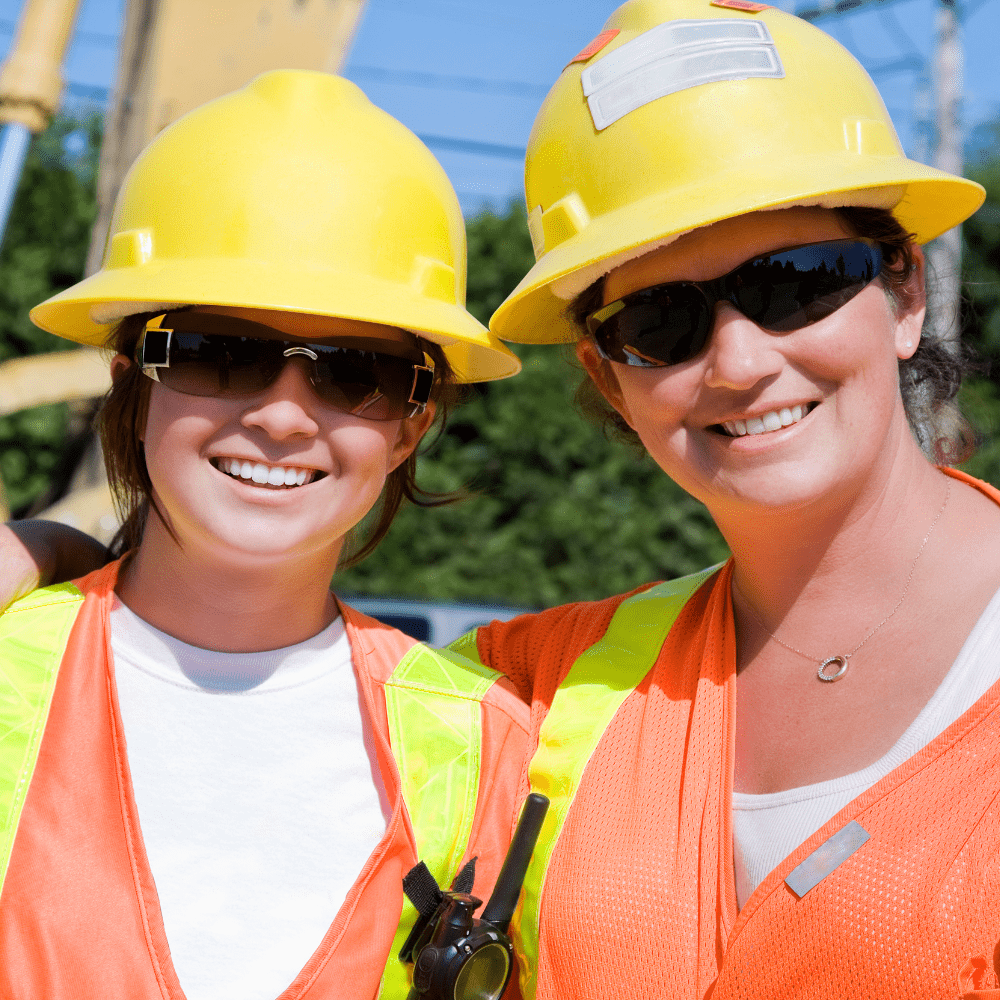 Two women in safety vests and hard hats in the construction industry.
