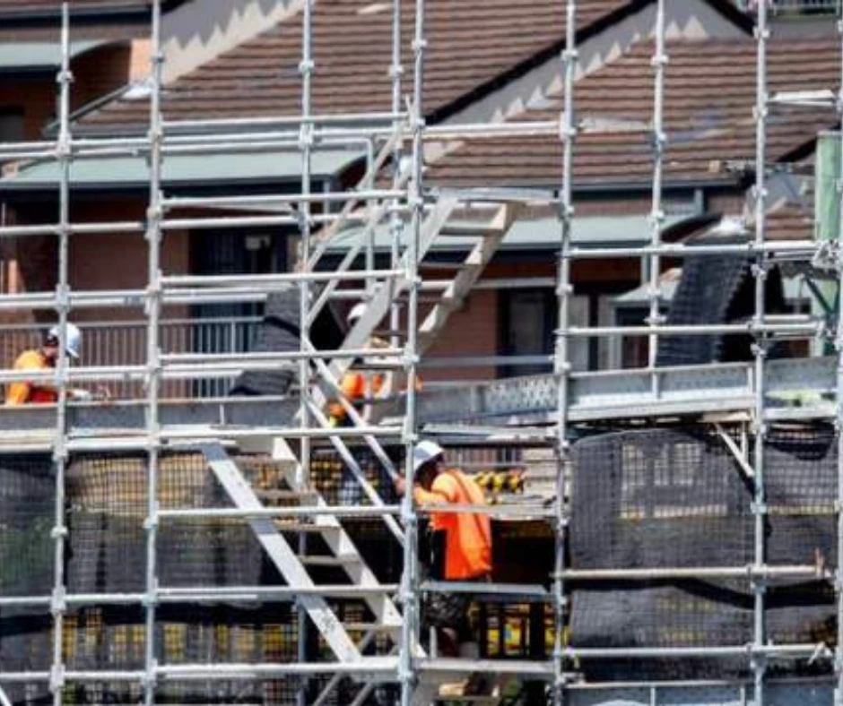 Construction workers using scaffold access systems while performing work at heights, highlighting fall-prevention structures on a multi-level job site.