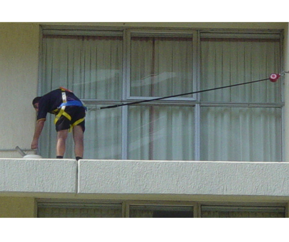 Work at heights safety demonstration showing a worker on an elevated ledge using a harness and anchor line, highlighting an example of unsecured positioning risk