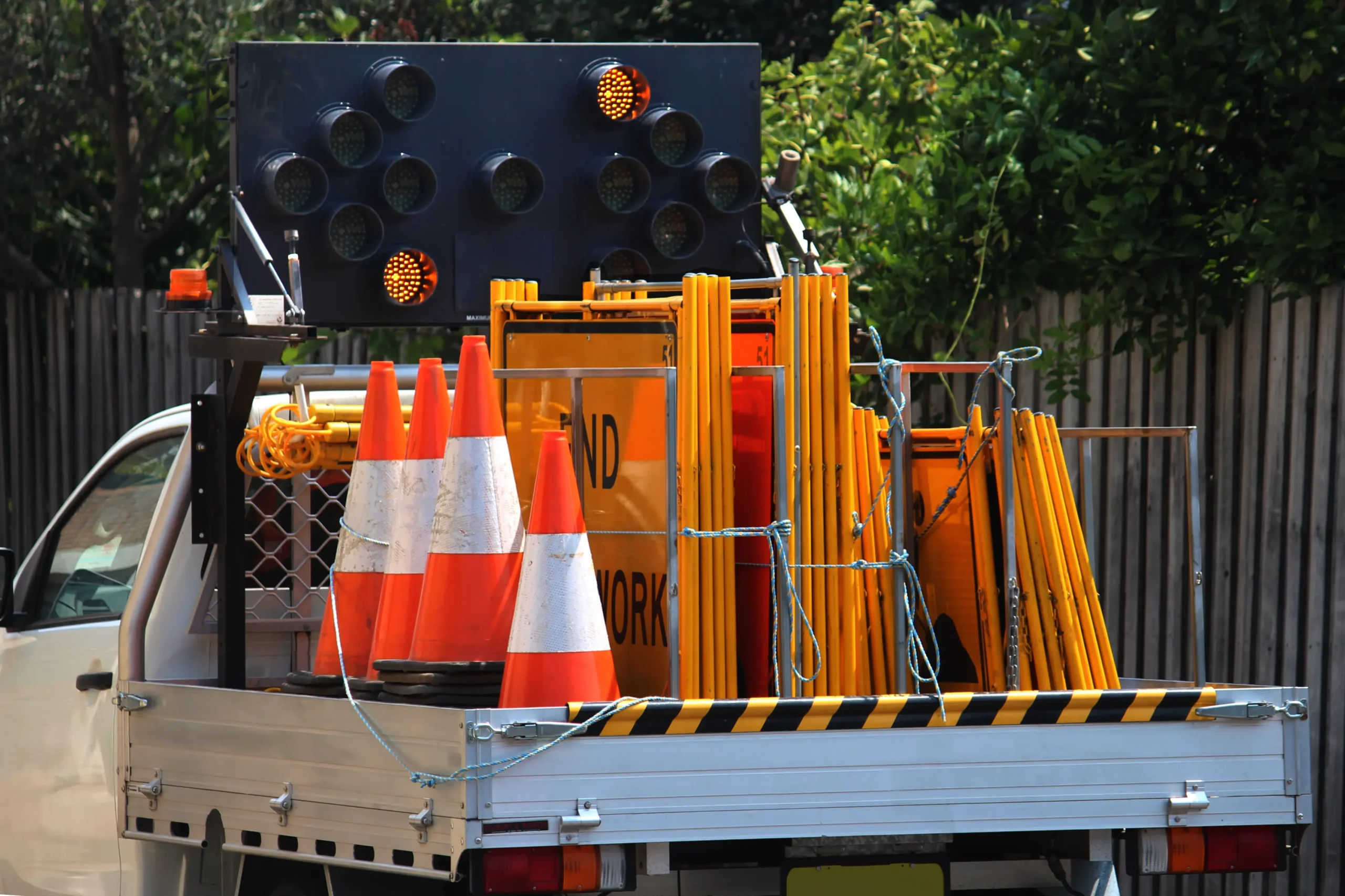 Traffic management implementation (TMI) setup equipment on utility vehicle with cones, barriers, and portable traffic lights for roadwork safety in Queensland