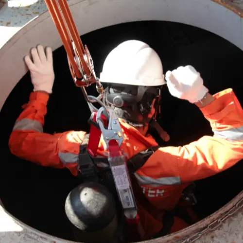 Confined space worker entering underground access hatch using safety harness and gas monitoring equipment during confined spaces training in Queensland.