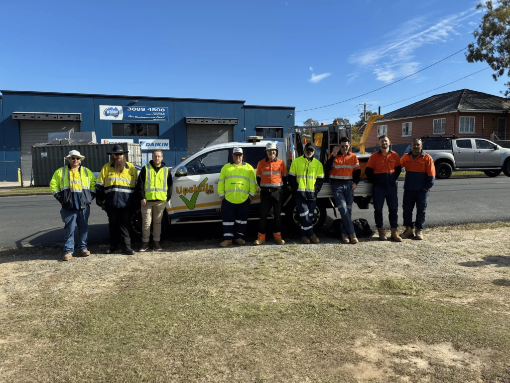 Group of traffic control trainees in high-visibility workwear standing beside an Upskills QLD training vehicle outside a commercial building in Brisbane Queensland.